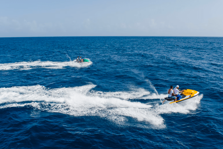 Two people riding jet skis on the ocean under a clear sky.