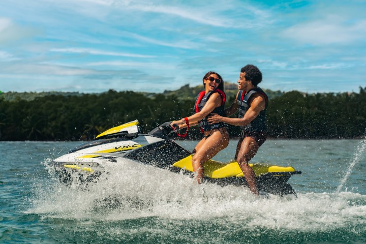 Two people smiling while riding a yellow jet ski on the water.