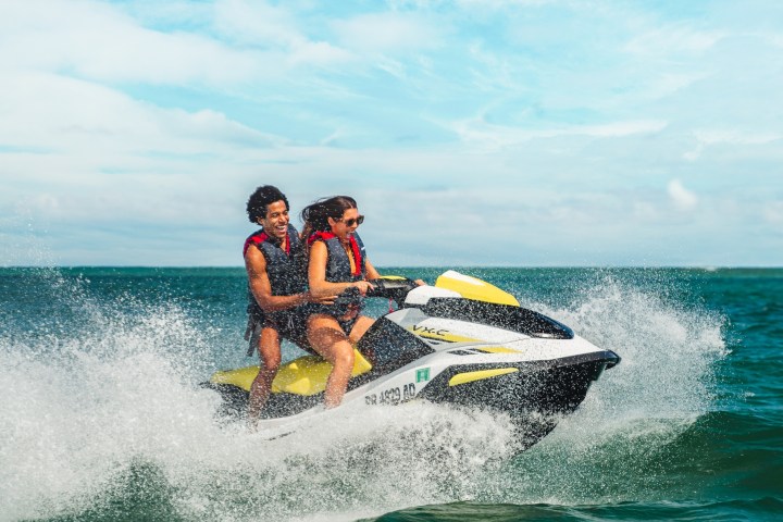 Two people riding a jet ski on ocean waves under a blue sky.