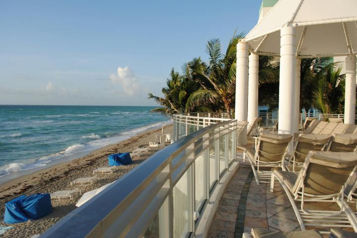 Beach view with lounge chairs, palm trees, and railing by the ocean.